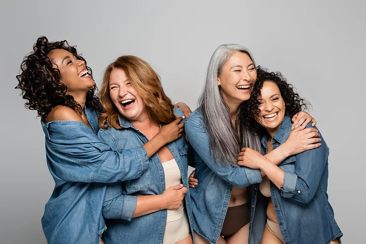 Four women in denim shirts share a joyful moment, laughing together.